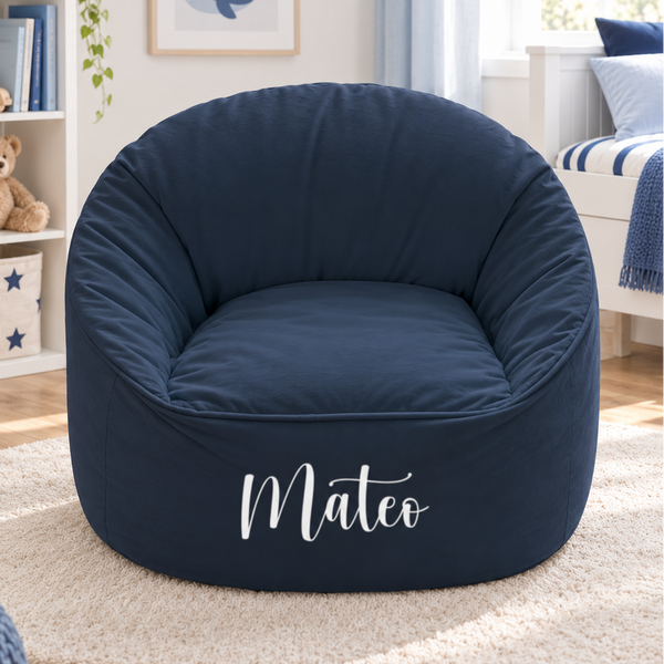 A navy blue fabric bean bag chair with the name 'Mateo' printed in white script on the front, set on a cream shag rug in a styled children's room.